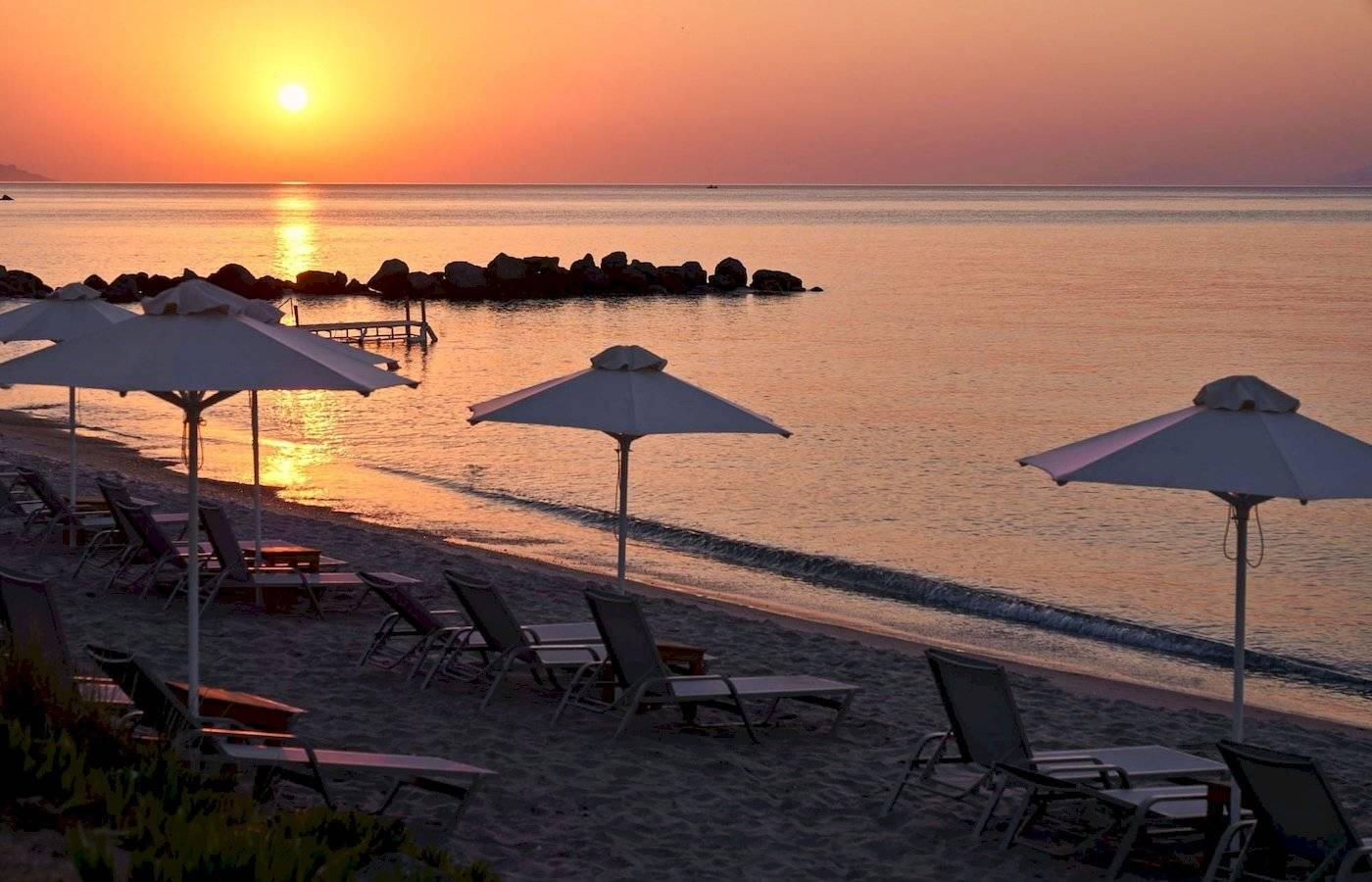 Sonnenuntergang am Strand des Atlantica Beach Resort Kos mit vielen Sonnenschirmen und Liegestühlen