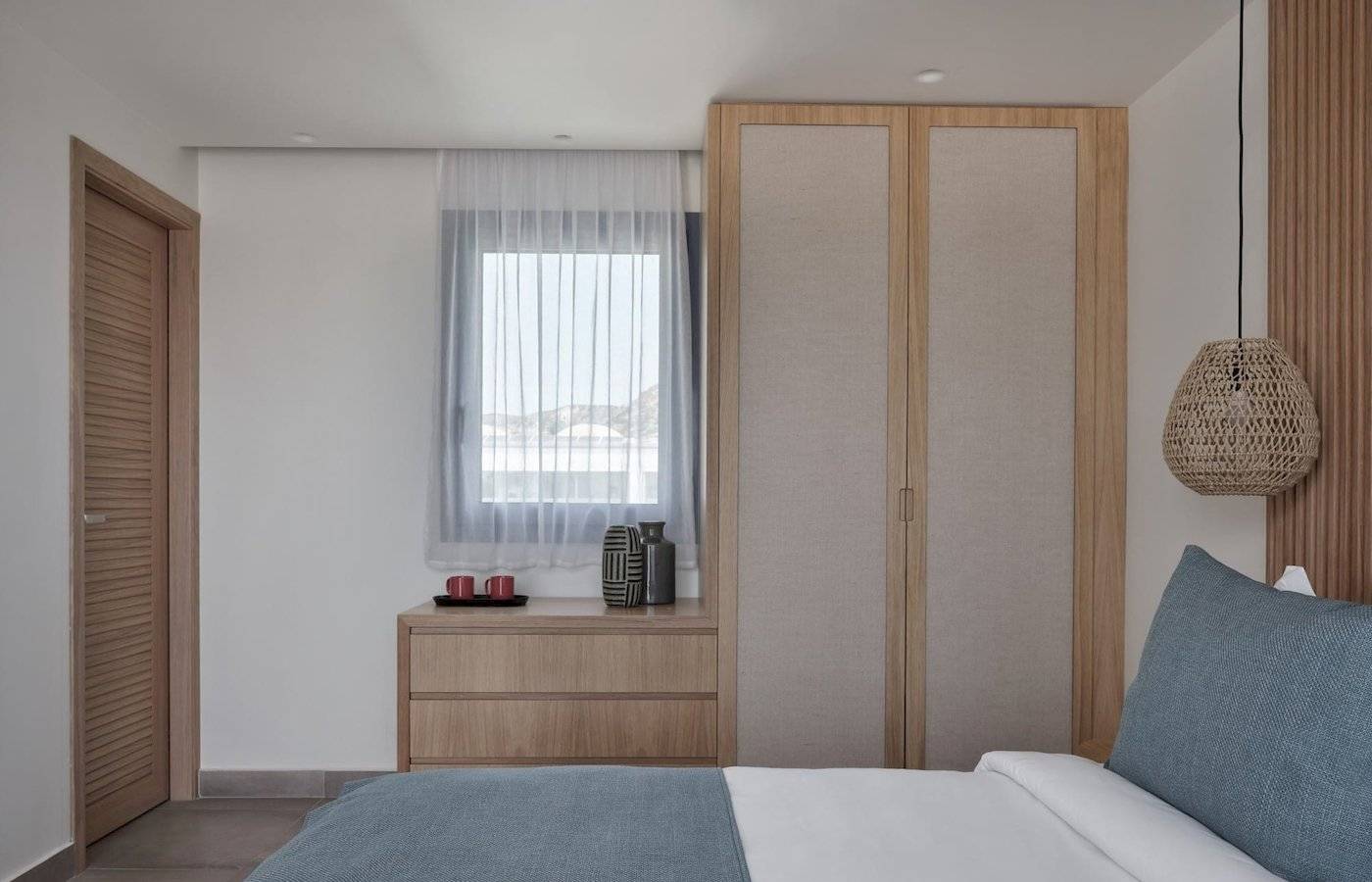 Inneneinrichtung eines Schlafzimmers im Atlantica Beach Resort Kos mit Doppelbett, Nachttisch, Kleiderschrank und Fenster mit Vorhängen.