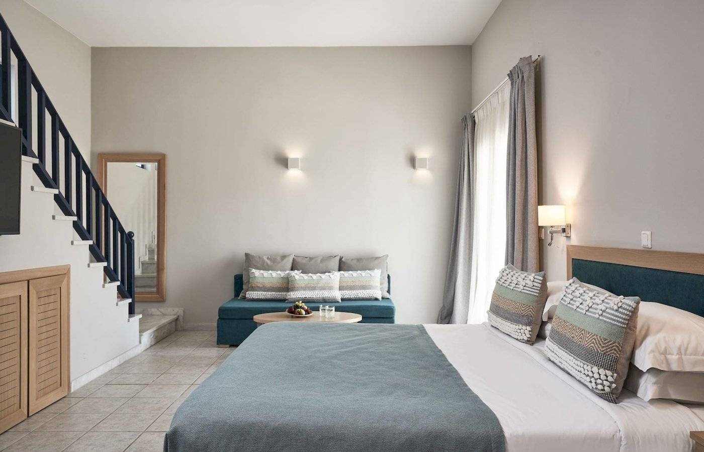 Schlafzimmer im Atlantica Beach Resort Kos mit einem Bett, einem Couchtisch, einer Kommode und einer Treppe.