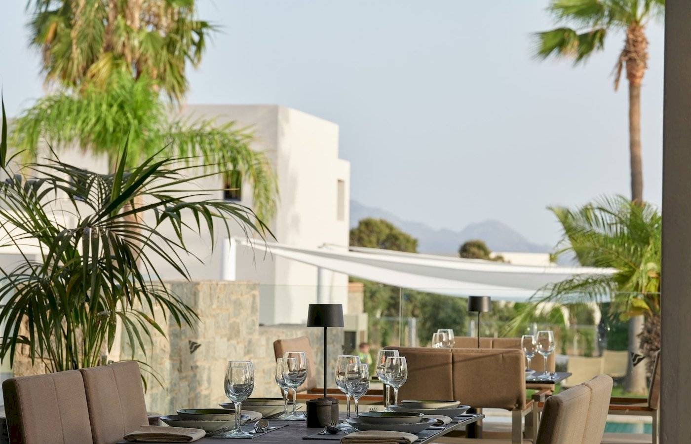 Restauranttisch im Atlantica Beach Resort Kos mit Blick auf Palmen und Gebäude.