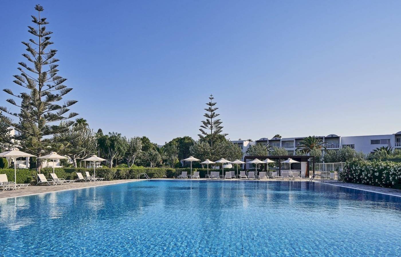 Außenpoolbereich des Atlantica Beach Resort Kos mit weißen Liegestühlen und Sonnenschirmen.