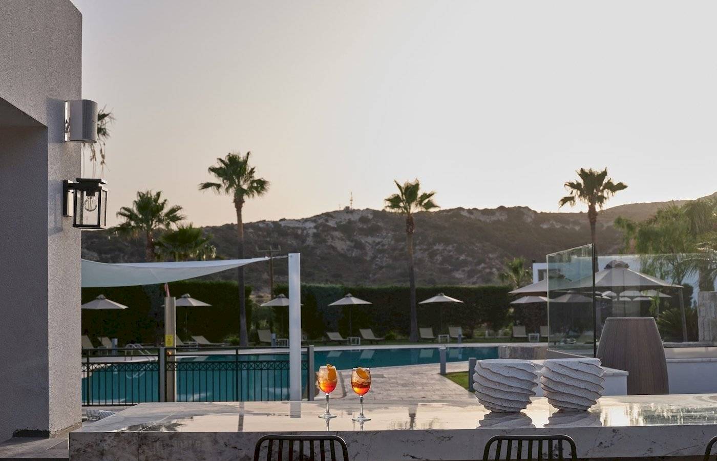 Abendlicher Blick auf den Pool des Atlantica Beach Resort Kos mit Cocktails und Palmen.