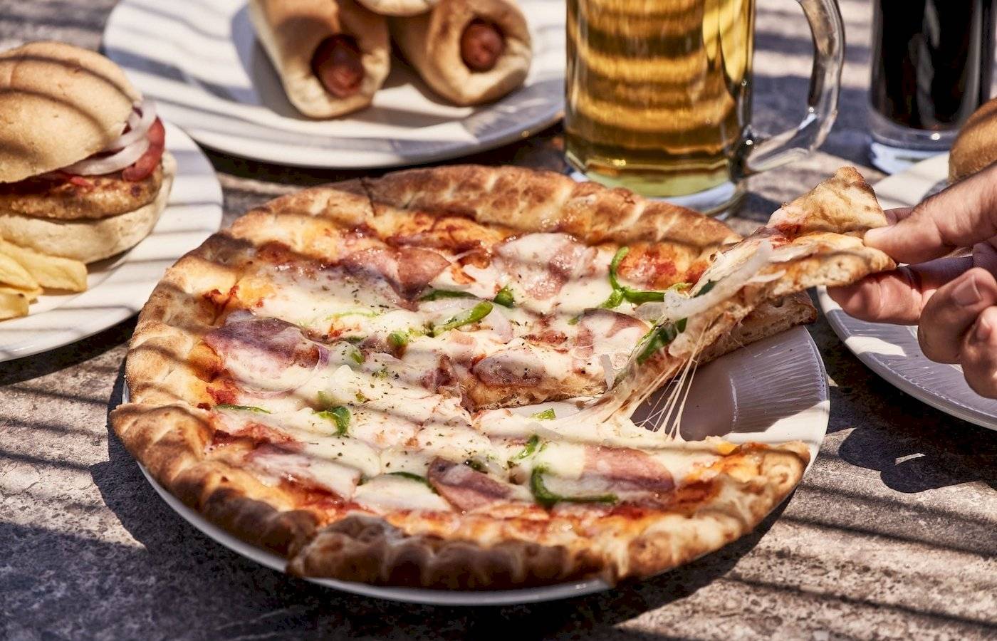 Tisch mit einer geschnittenen Pizza, Bier, alkoholfreien Getränken und Sandwiches.