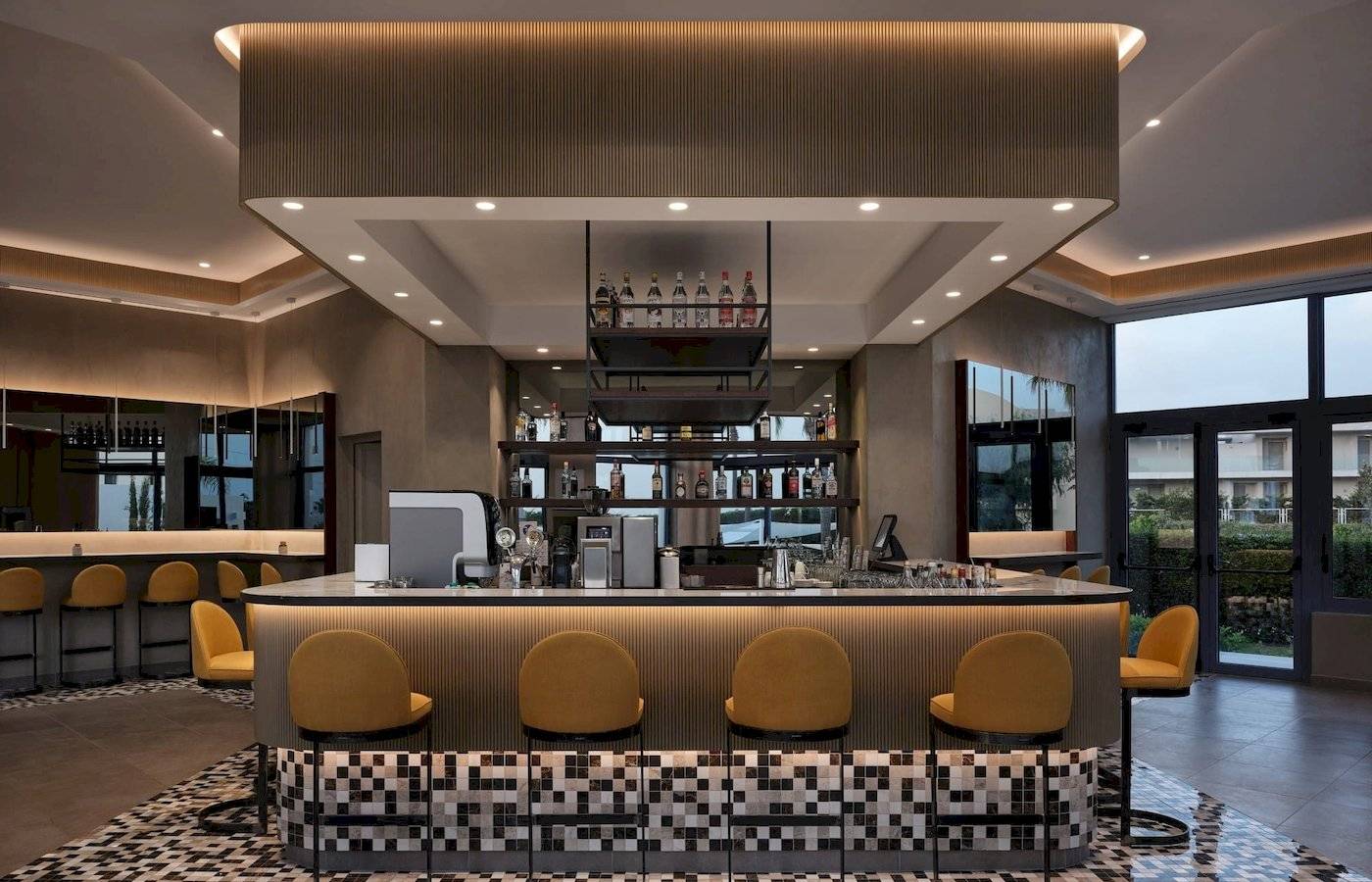 Rezeption Bar im Atlantica Beach Resort Kos mit gemustertem Boden und gelben Stühlen.