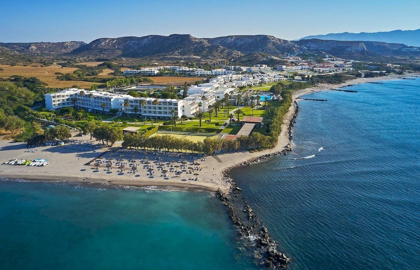 Gesamtansicht des Atlantica Beach Resort Kos am Strand mit vielen Liegestühlen und Hotelgebäuden.