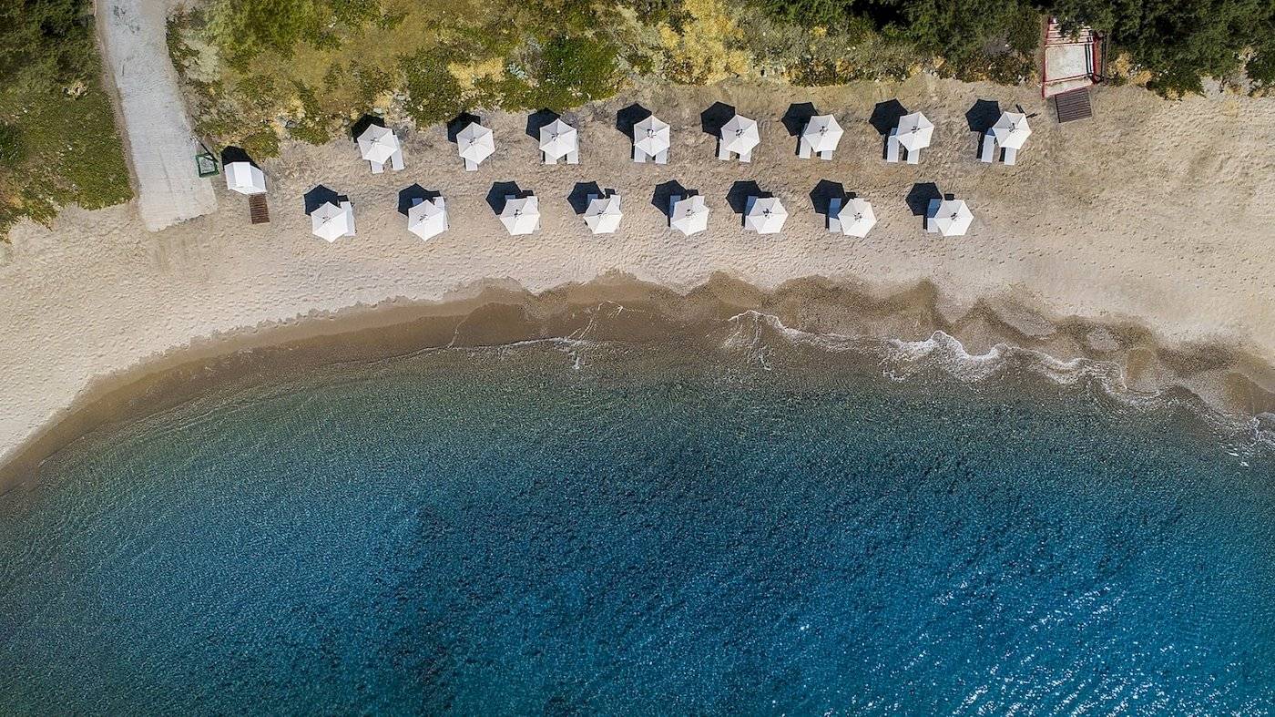 Luftaufnahme des Atlantica Beach Resort Kos mit vielen weißen Sonnenschirmen am Strand und blauem Meer.