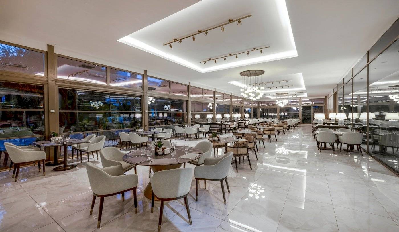 Innenbereich des Nirvana Cosmopolitan Hotels mit vielen Tischen und Stühlen, hängenden Kronleuchtern und großen Fenstern.