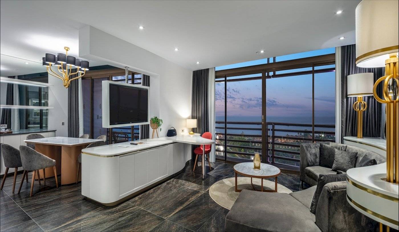 Modernes Hotelzimmer mit Meerblick, Tisch, Stühlen, Sofa, Fernseher und Lampen.