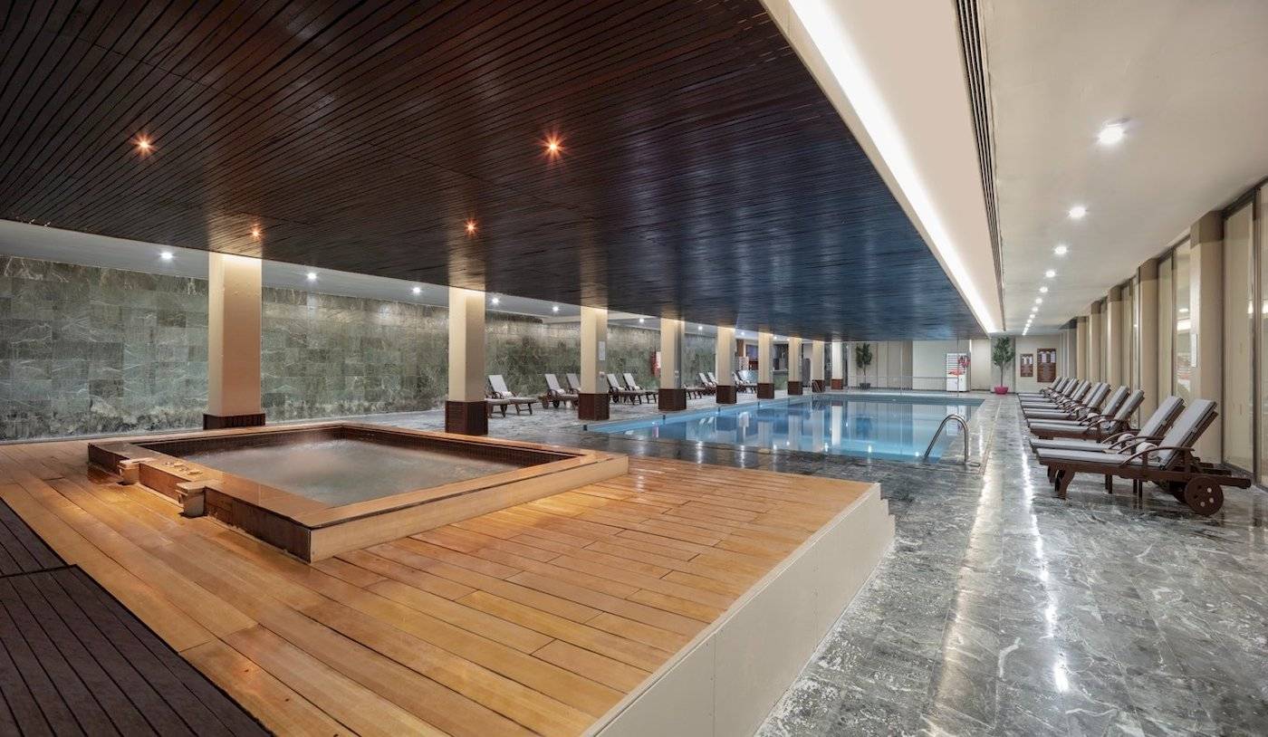 Innenpoolbereich des Nirvana Cosmopolitan Hotels mit Holzboden, Sitzliegen und einer großen Poolfläche.