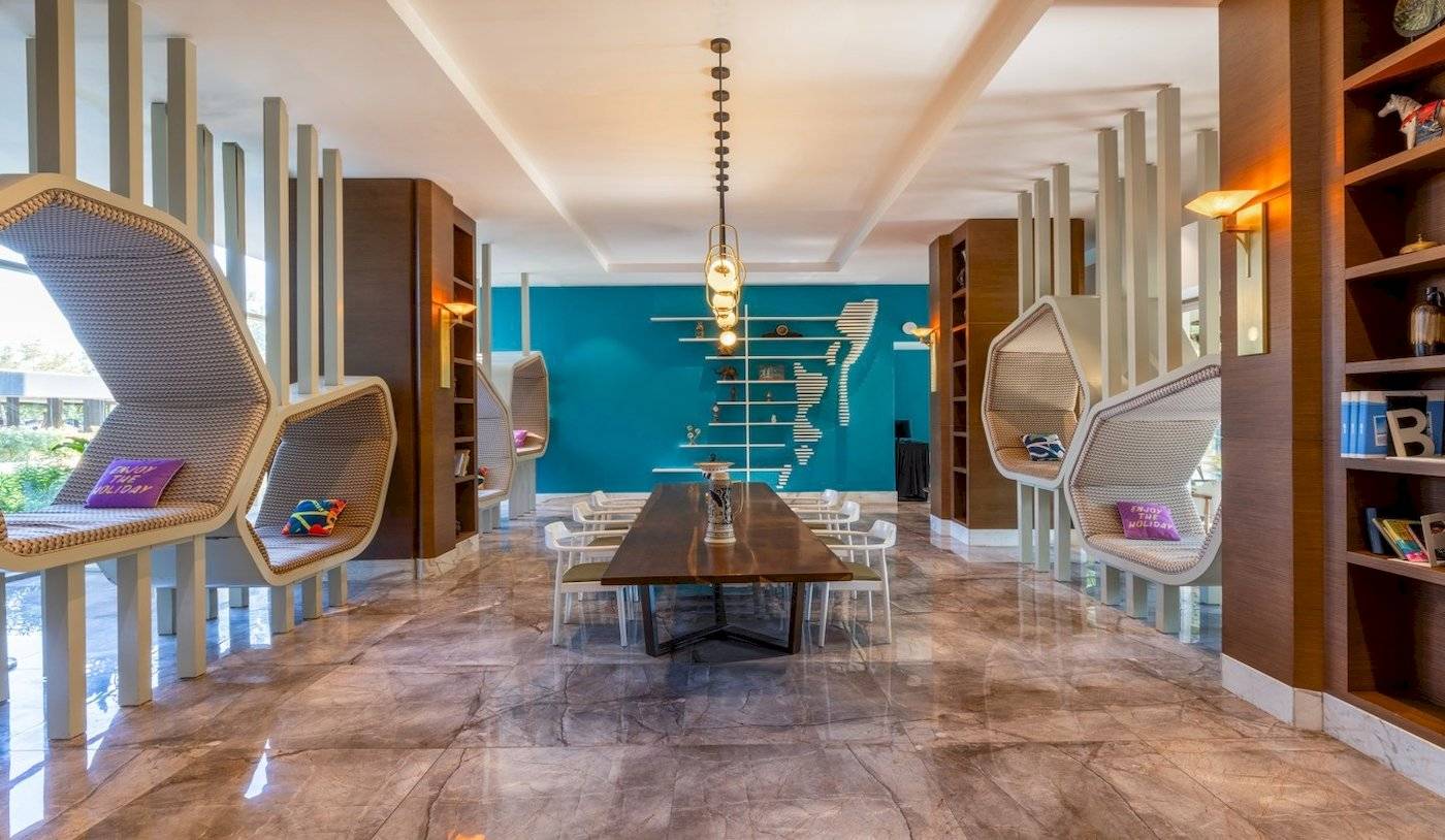 Innenansicht des Nirvana Cosmopolitan Hotels, zeigt einen großen Loungebereich mit einem Tisch und Sesseln, umgeben von blauen Wänden und modernen Möbeln.