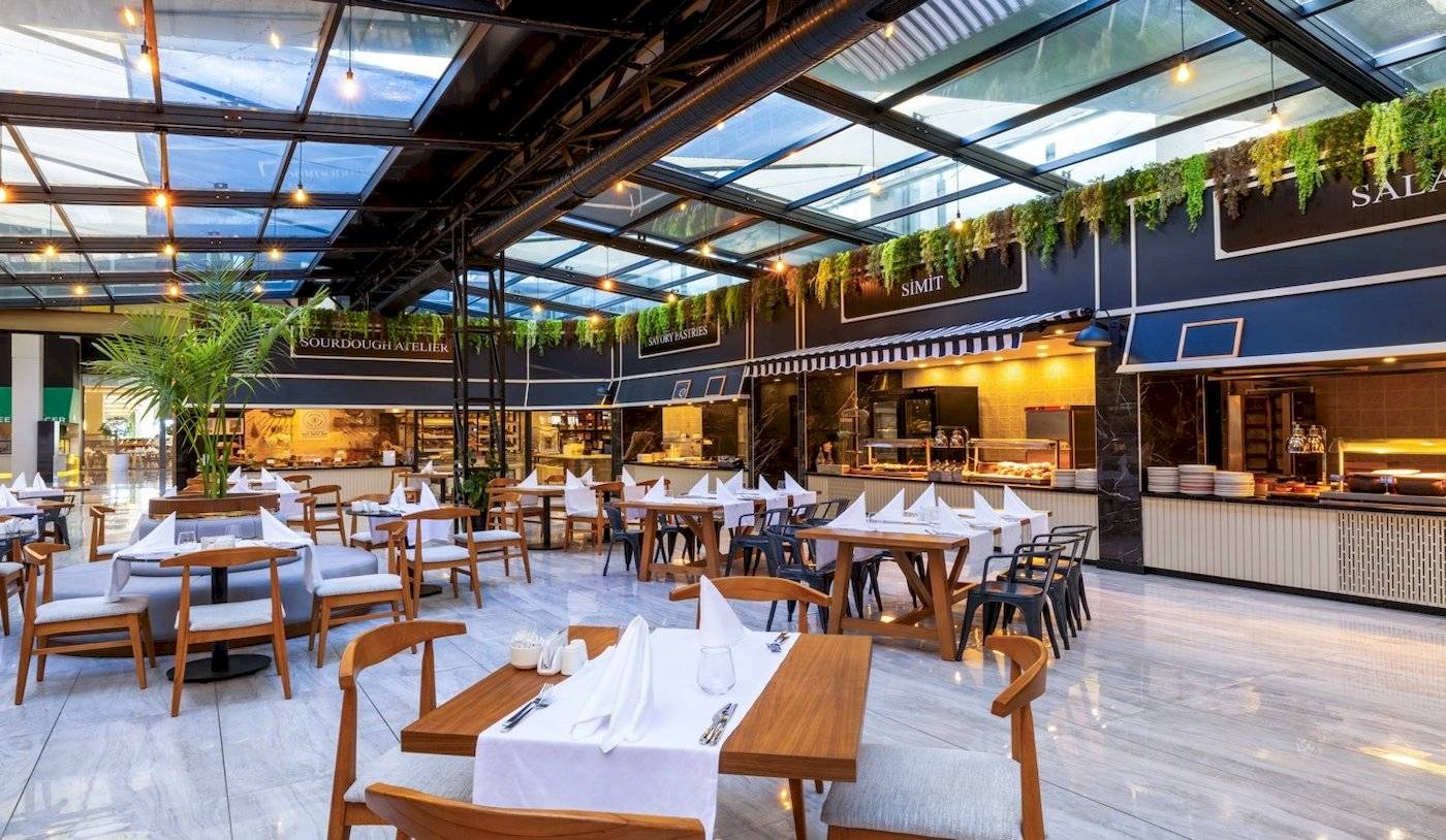 Innenansicht des Restaurants im Nirvana Cosmopolitan Hotel mit Tischen, Stühlen und einer Theke.