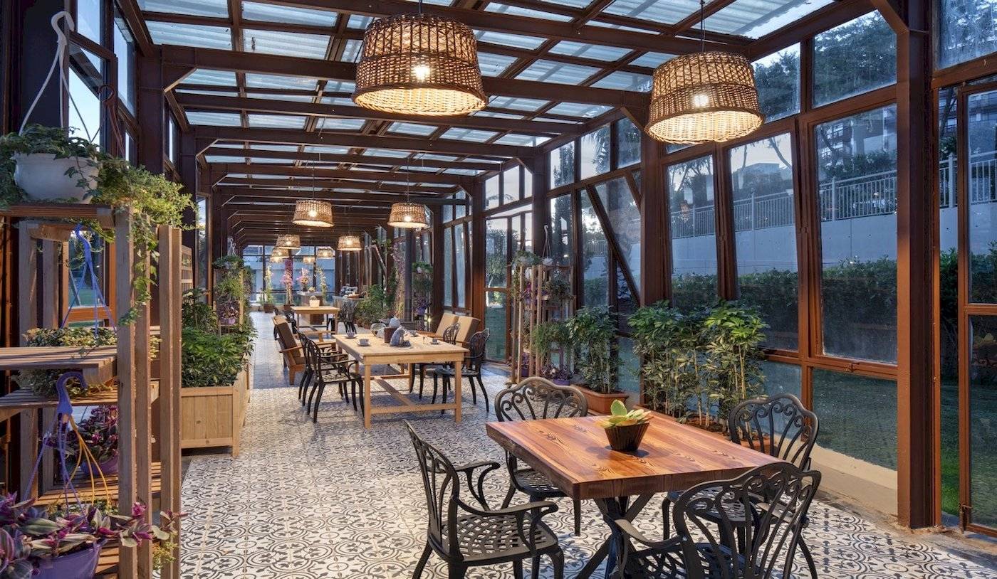 Innenansicht der Terrasse des Nirvana Cosmopolitan Hotels mit Tischen, Stühlen und Pflanzen.