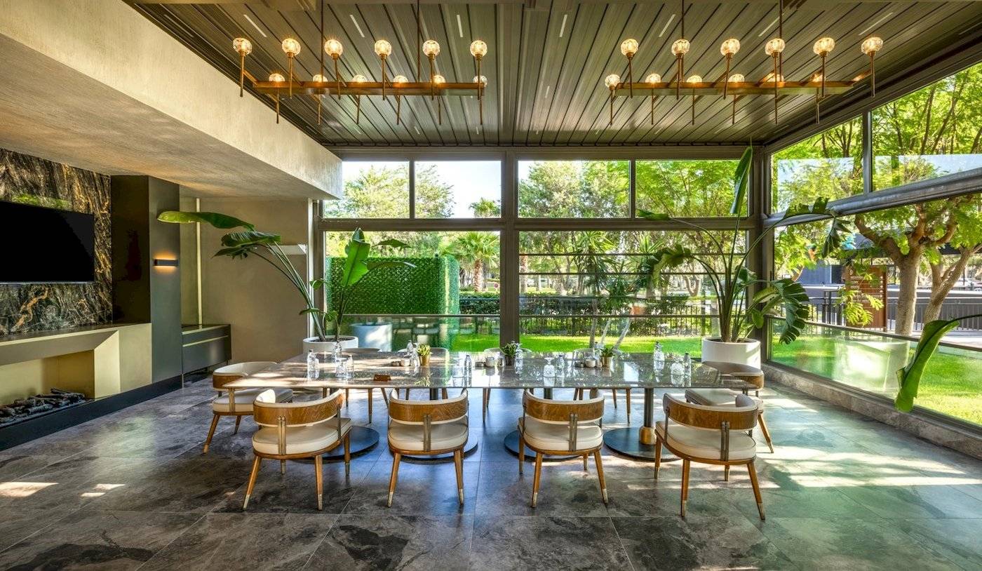 Ein Speisebereich im Nirvana Cosmopolitan Hotel mit einer grossen Tischplatte, Holzstühlen und grossen Fenstern.