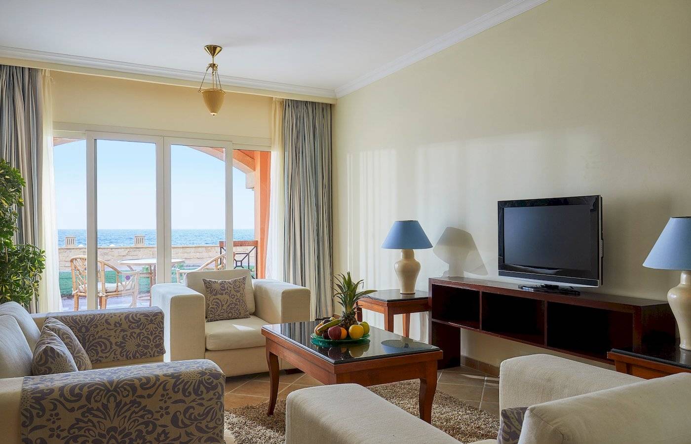 Wohnzimmer im Jaz Grand Marsa Hotel mit Meerblick, Fernseher, Sofas und Tisch mit Früchten.