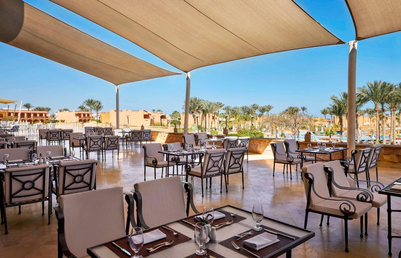 Außenbereich des Jaz Grand Marsa Hotels mit Tisch und Stühlen unter Sonnenschirmen.