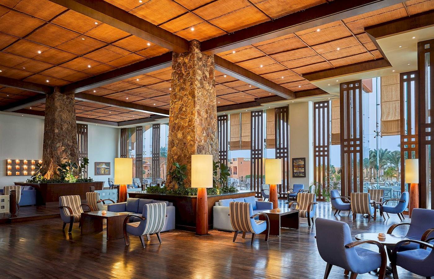 Innenansicht der Lobby im Jaz Grand Marsa Hotel mit blauen Stühlen und Holzböden.