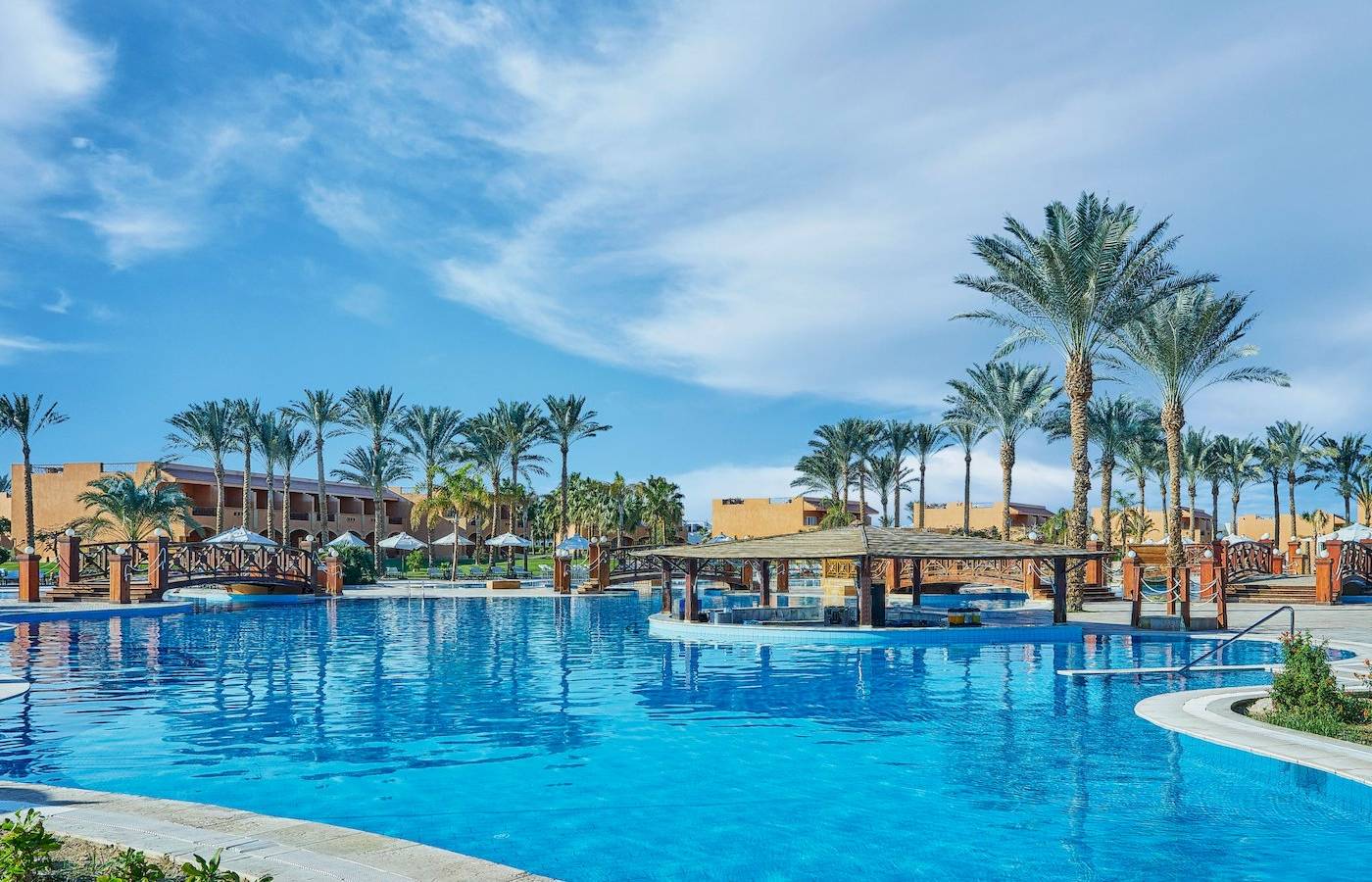 Der Pool des Jaz Grand Marsa Hotels mit Brücke und Palmen im Hintergrund.