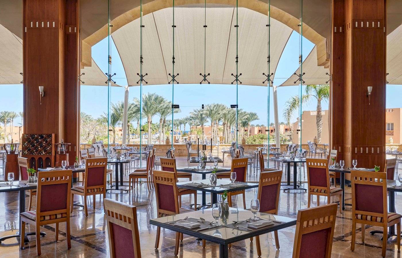 Restaurantbereich im Jaz Grand Marsa Hotel mit Glaswänden und Blick auf Palmen.