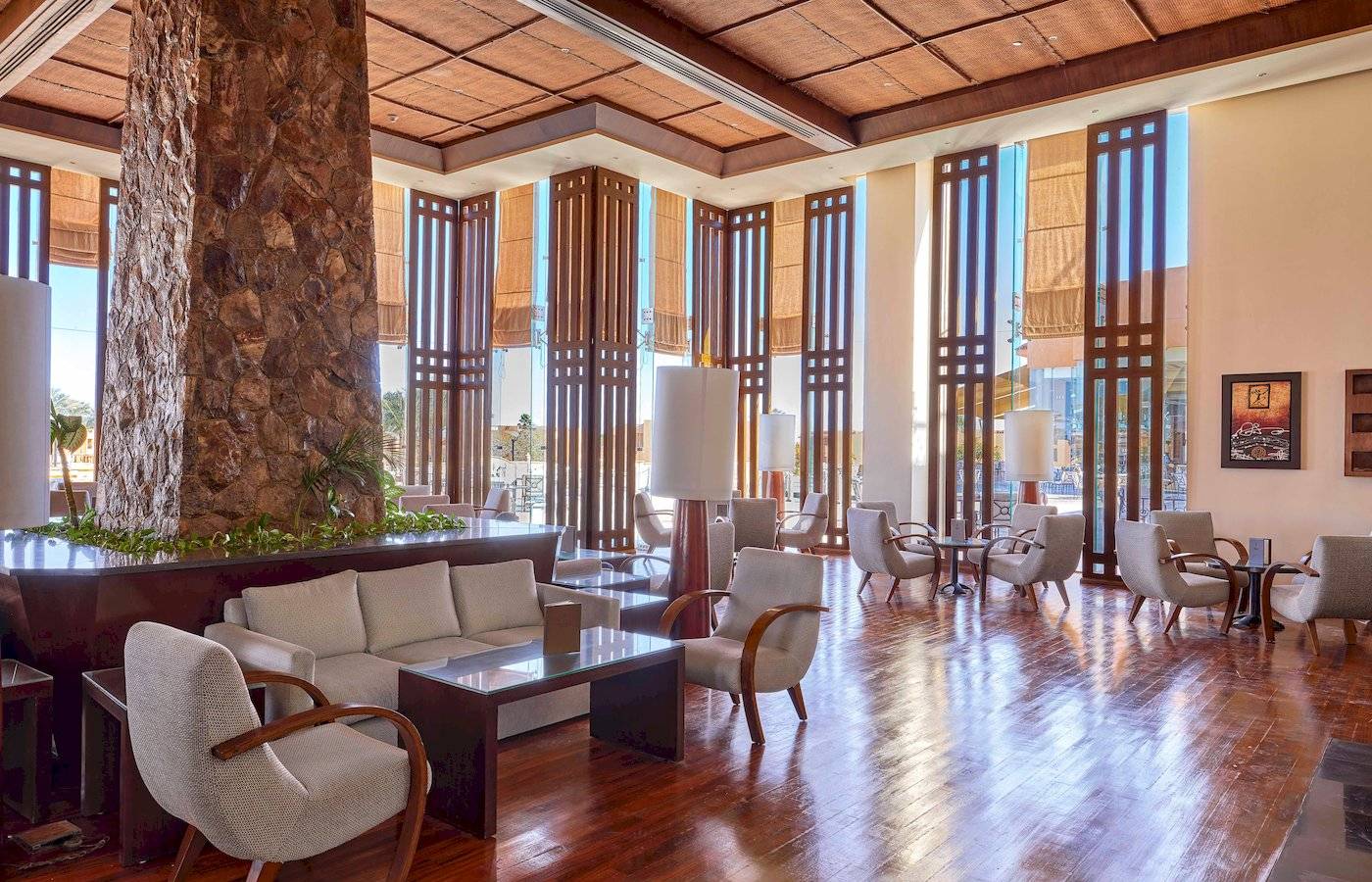 Innenansicht der Lobby des Jaz Grand Marsa Hotels mit Holzboden, Möbeln und einer zentralen Säule.