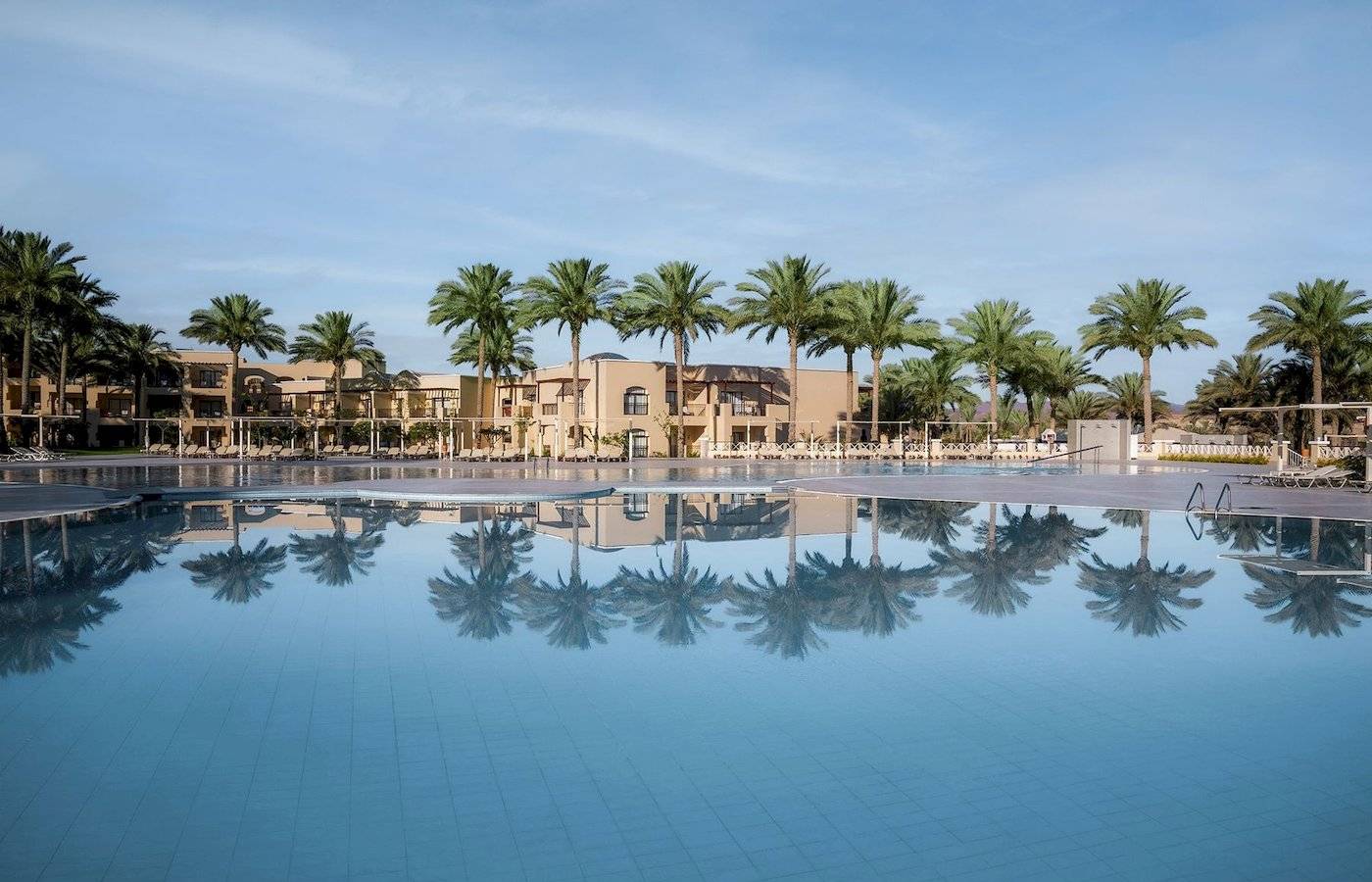 Außenpool des Jaz Lamaya Resorts mit Palmen und Hotelgebäuden im Hintergrund.