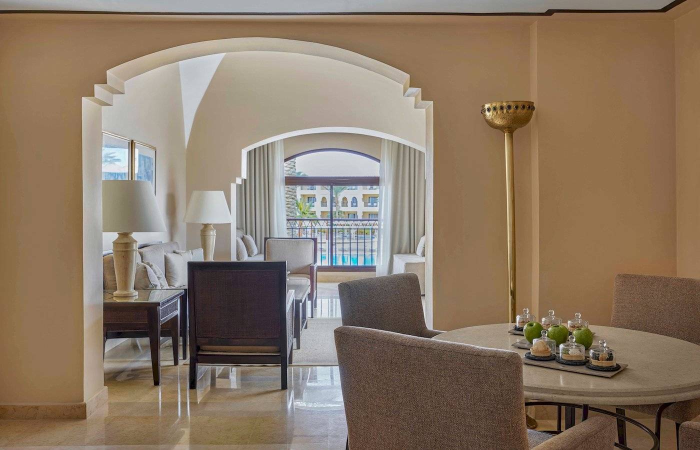 Innenansicht des Wohnbereichs im Jaz Lamaya Resort mit Tisch, Stühlen und Blick auf einen Swimmingpool.