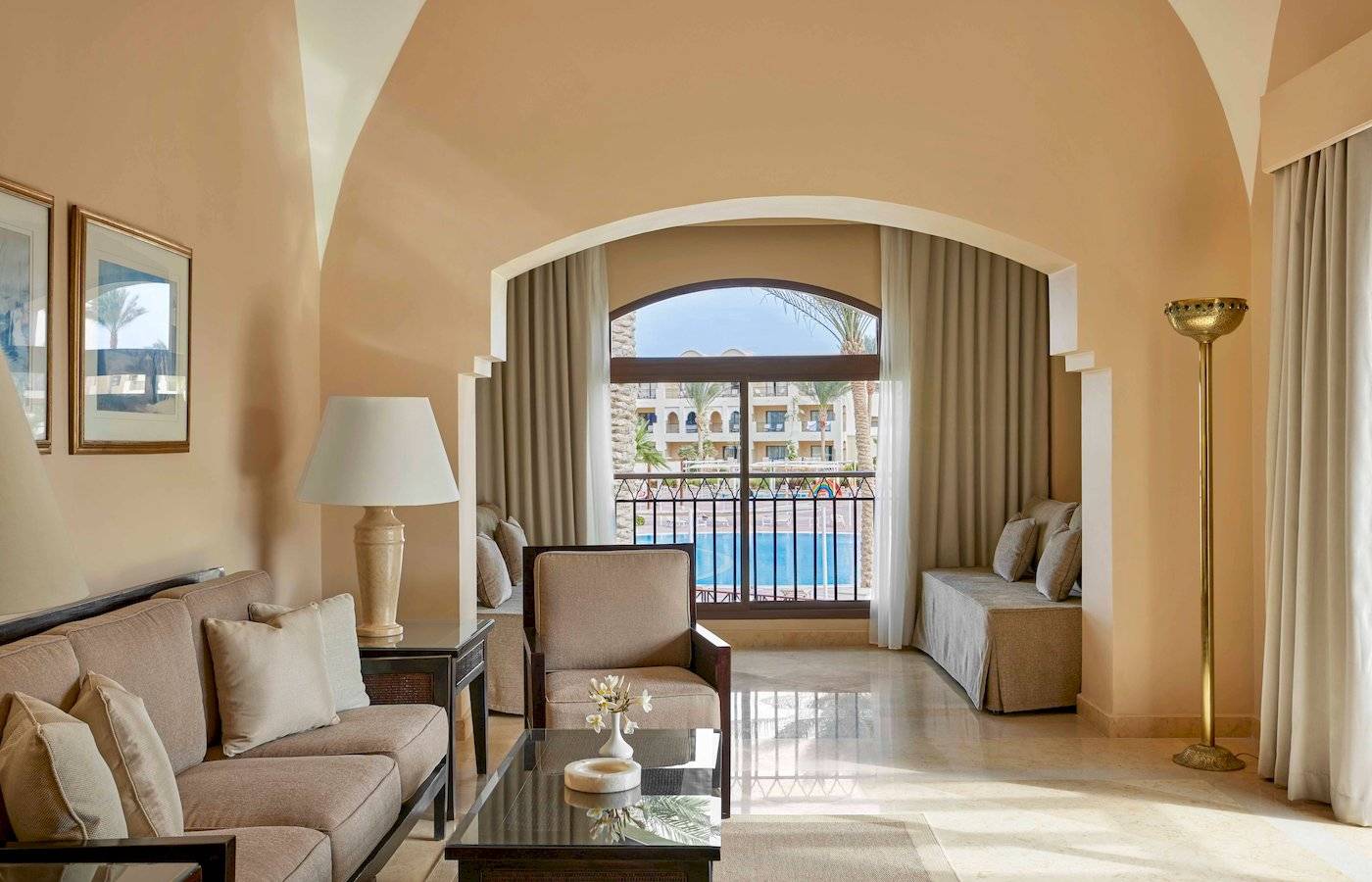 Wohnzimmer des Jaz Lamaya Resorts mit Sofa, Tisch, Lampe und Terrassenfenster mit Poolblick