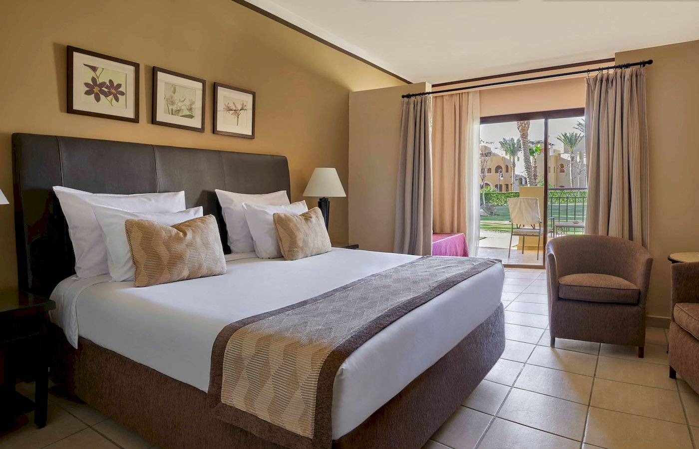 Schlafzimmer im Jaz Lamaya Resort mit Doppelbett, Kissen, Lampen und Zugang zu einer Terrasse.