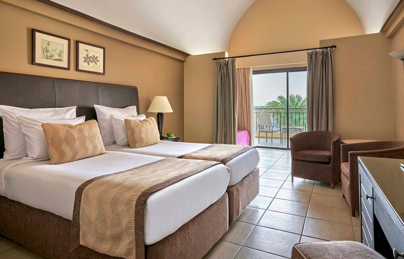 Doppelzimmer im Jaz Lamaya Resort mit zwei Betten, Sessel, Schreibtisch und Balkon mit Meerblick.