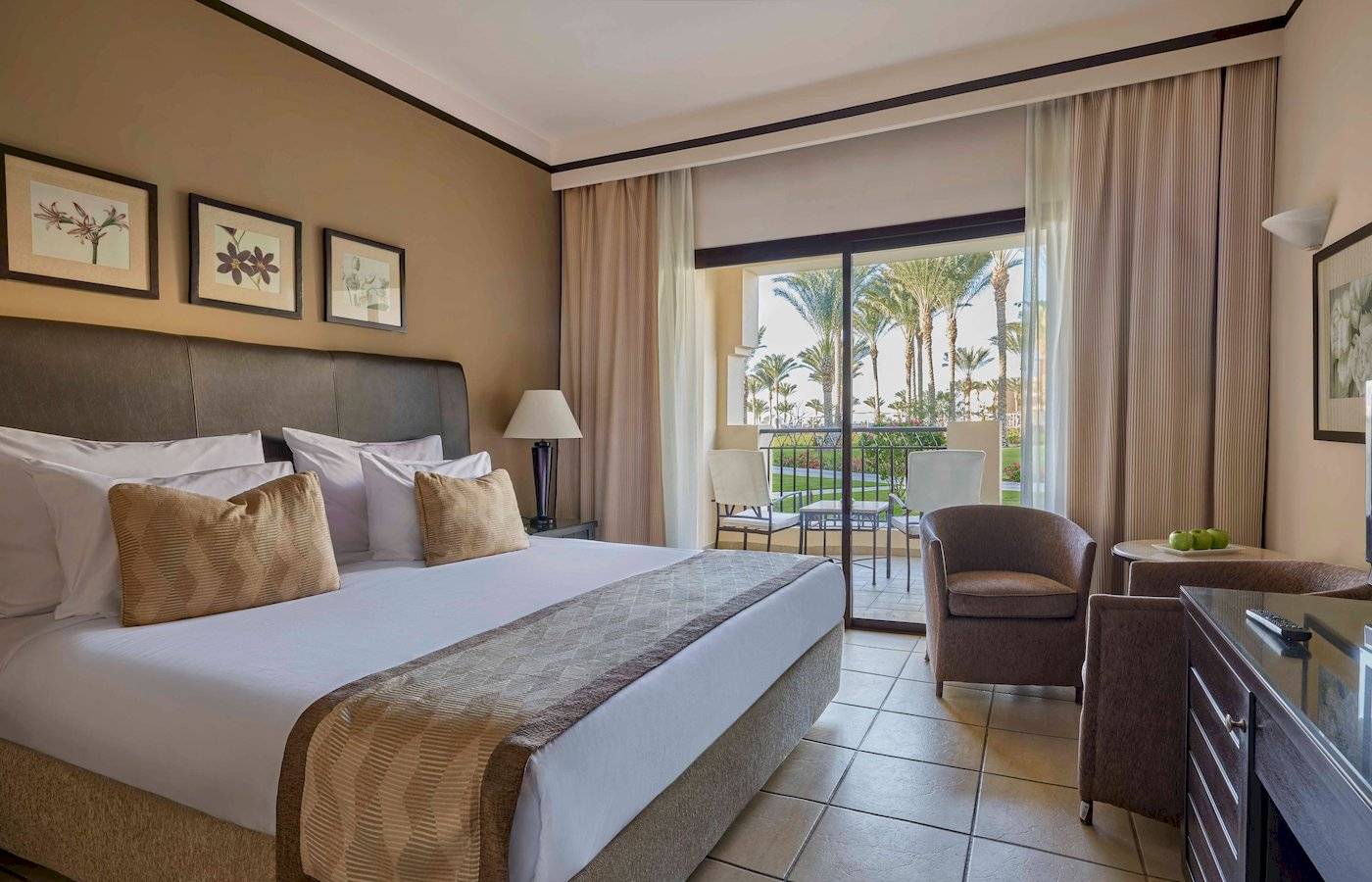 Schlafzimmer im Jaz Lamaya Resort mit einem großen Bett, Kissen und einem Balkon mit Blick auf Palmen.