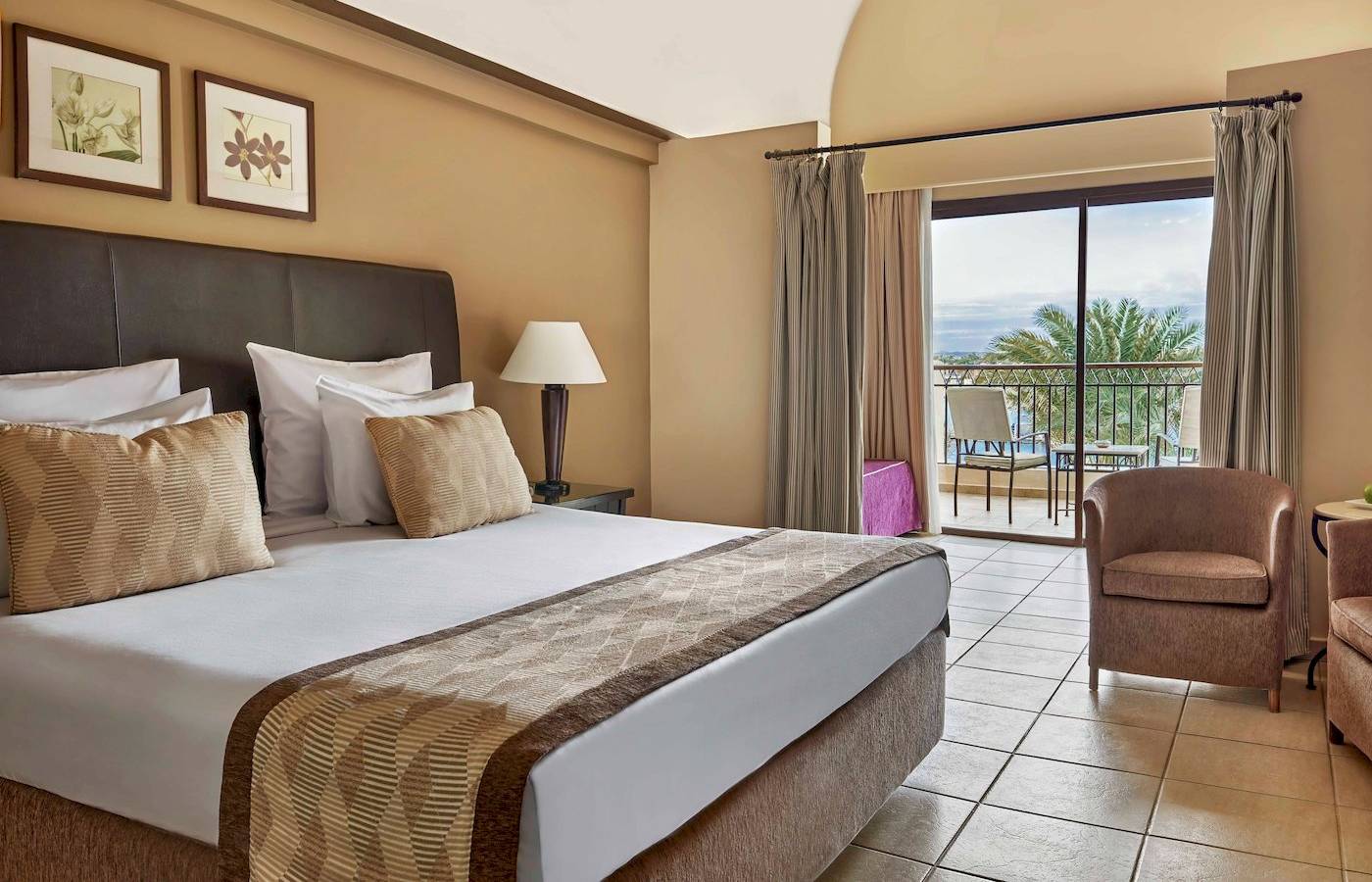 Doppelzimmer im Jaz Lamaya Resort mit Bett, Kissen, Nachttisch, Lampe und Balkon.