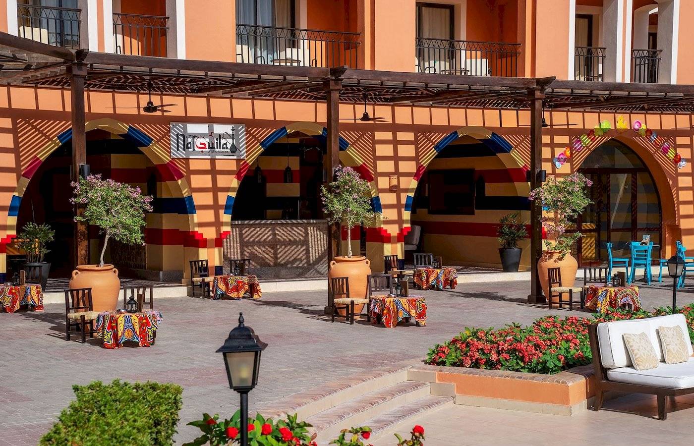 Lounge-Bereich des Jaz Lamaya Resorts mit bunten Tischen, Stühlen und Blumenbeeten.