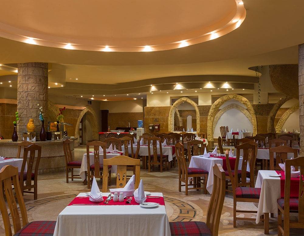 Innenansicht des Restaurants im Utopia Beach Club mit runden Tischen und Stühlen, dekorierten Tischen und architektonischen Bögen.