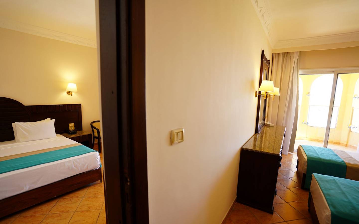 Innenansicht eines Hotelzimmers im Utopia Beach Club, mit einem Bett, einem Nachttisch und einer Terrasse.