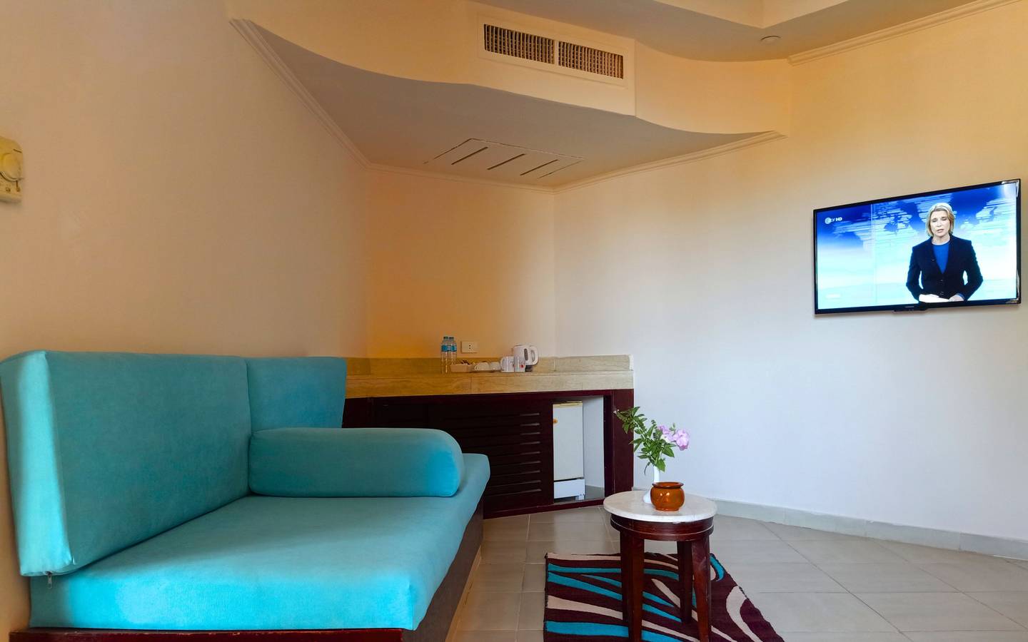 Wohnbereich im Utopia Beach Club Hotel mit blauem Sofa, Tisch, Fernseher und Blumen.