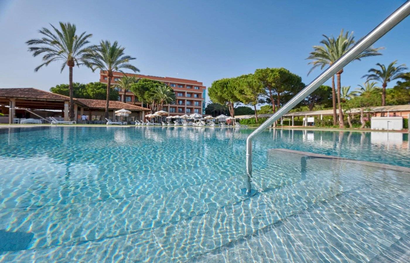 Außenpool des Hipotels Hipocampo Palace Hotels mit Sonnenliegen und Gebäude im Hintergrund.