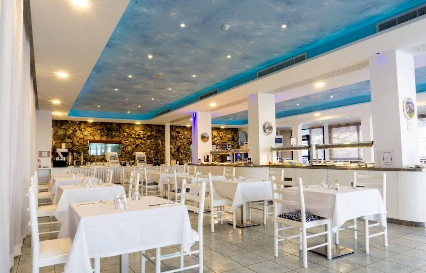 Innenbereich des Anonymous Beach Hotels mit blauem Himmel-Decke, weißen Tischen und Stühlen.