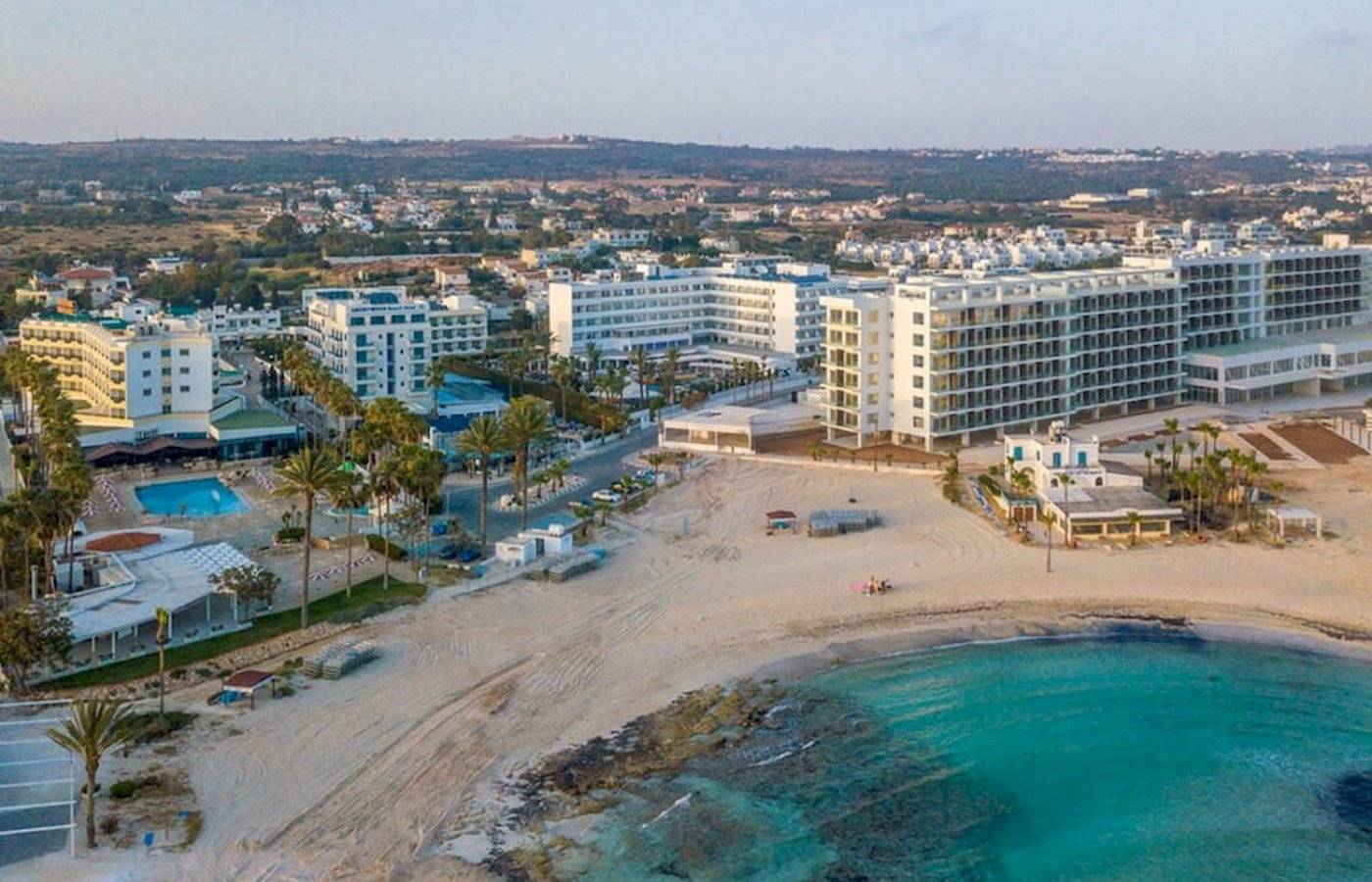 Luftaufnahme des Anonymous Beach Hotels mit mehreren Gebäuden, einem Pool und einer breiten Sandbucht.