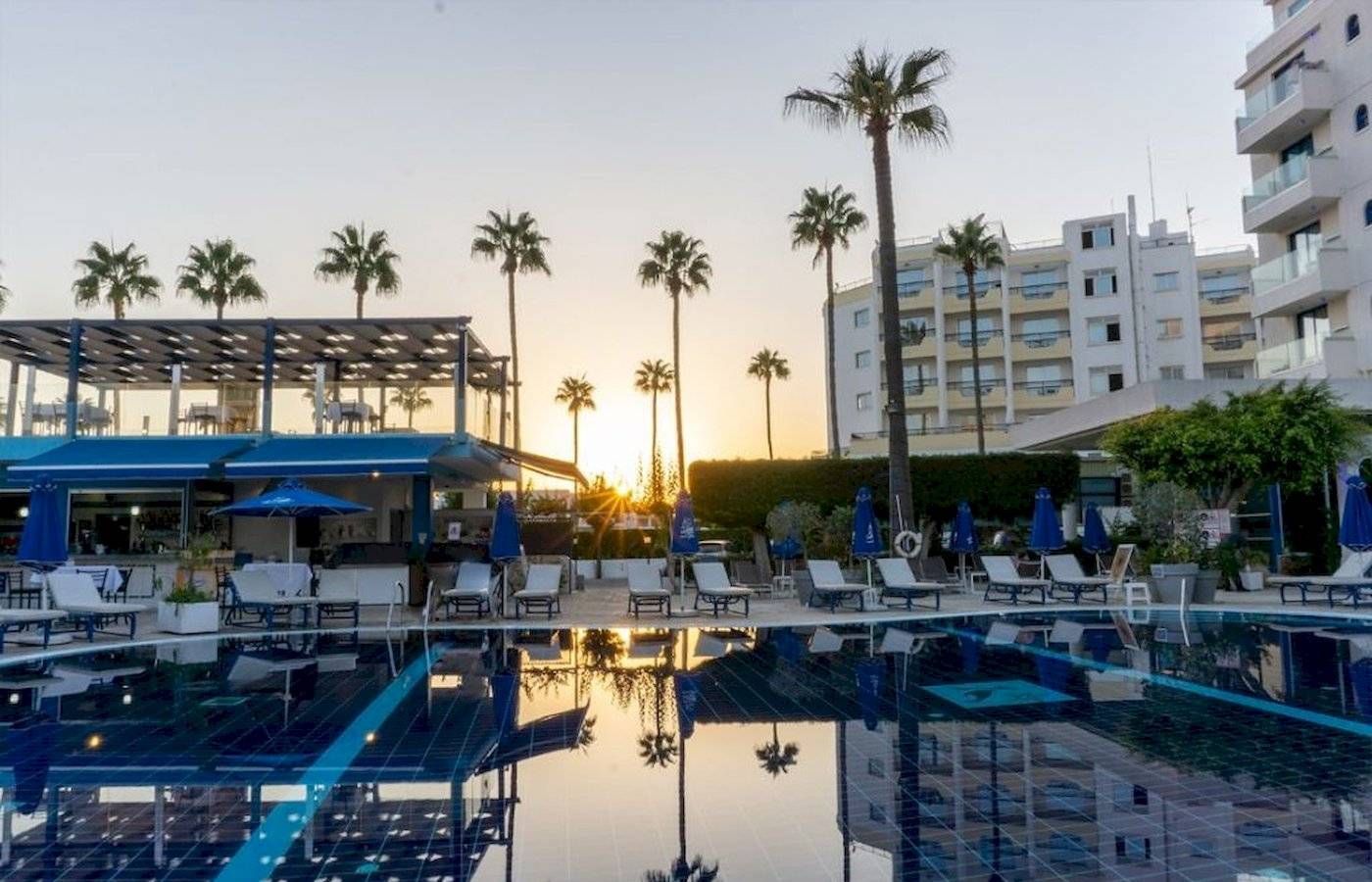 Der Swimmingpool des Anonymous Beach Hotels bei Sonnenuntergang mit Lounge-Stühlen und Palmen.