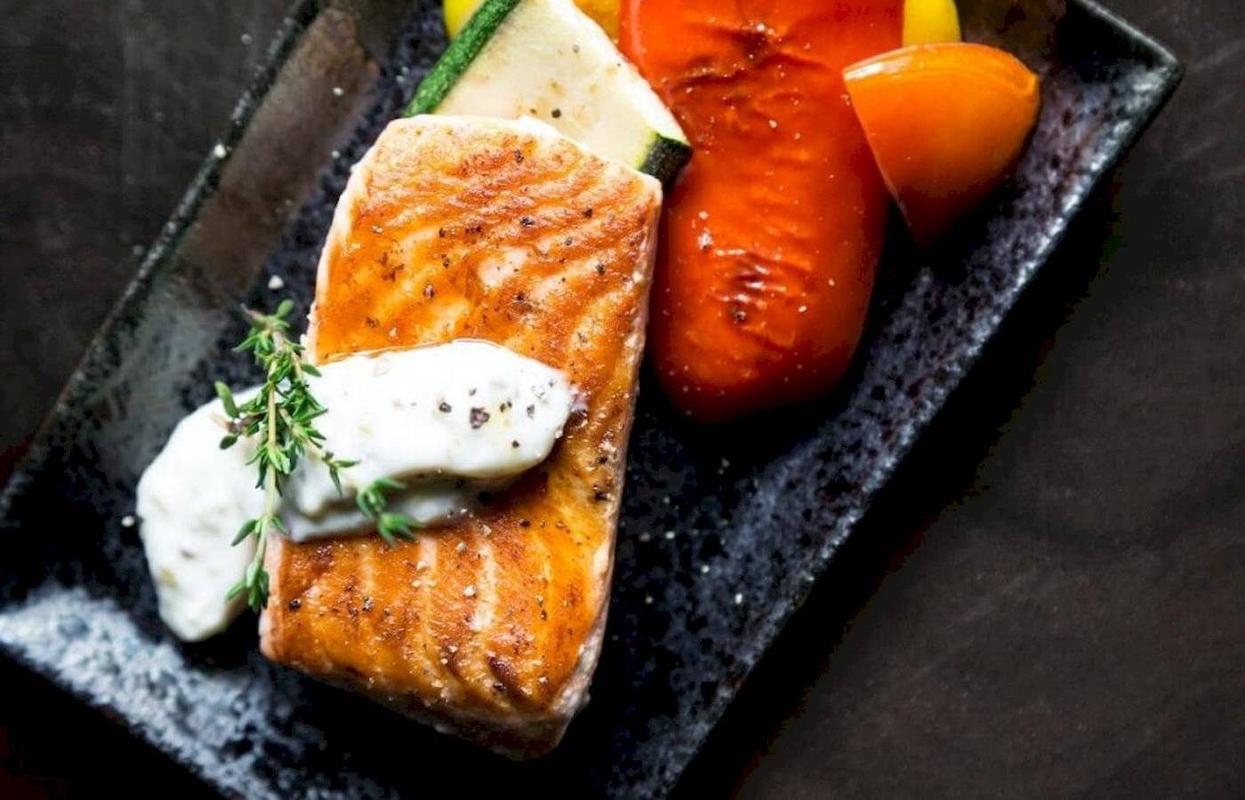 Gegrillter Lachs mit Gemüse und Kräutern auf einem schwarzen Teller.