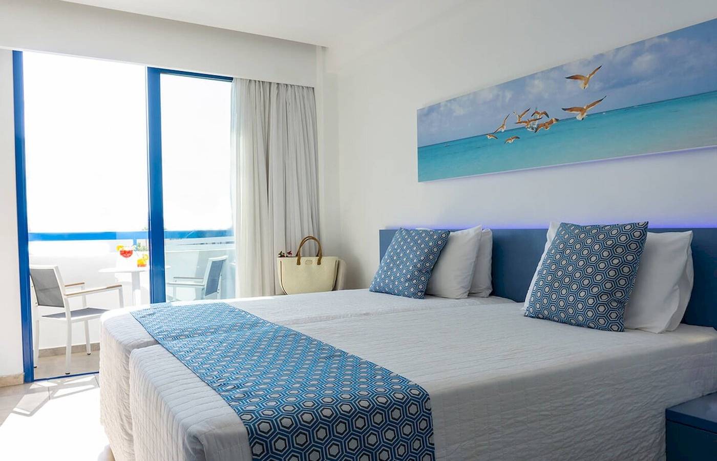 Doppelzimmer mit Meerblick im Anonymous Beach Hotel, mit zwei Betten, blauen Kissen und einem großen Wandbild von fliegenden Vögeln.