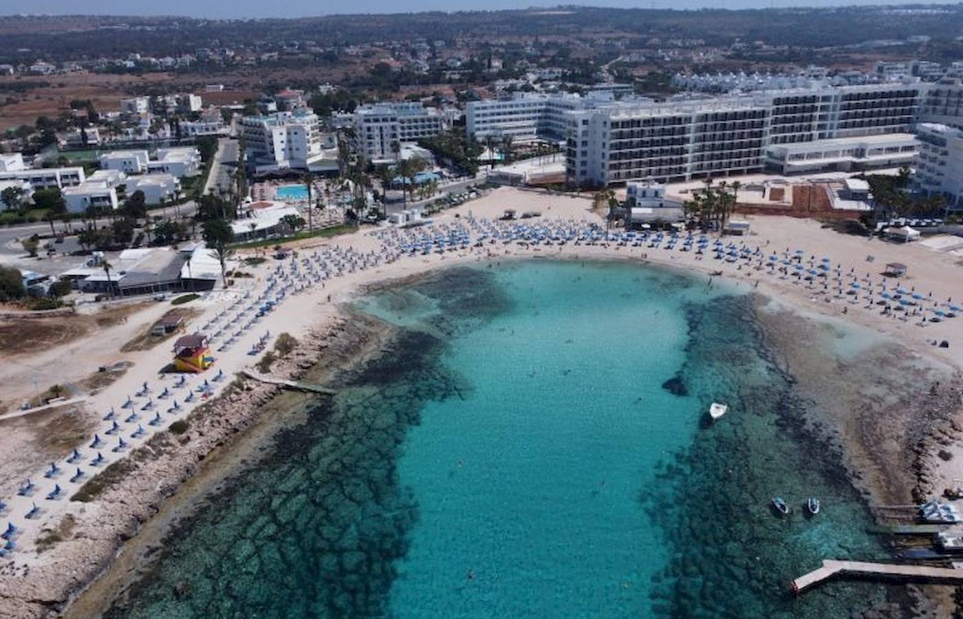 Luftaufnahme des Anonymous Beach Hotels, das an einen Strand angrenzt mit vielen Sonnenliegen und blauem Wasser.