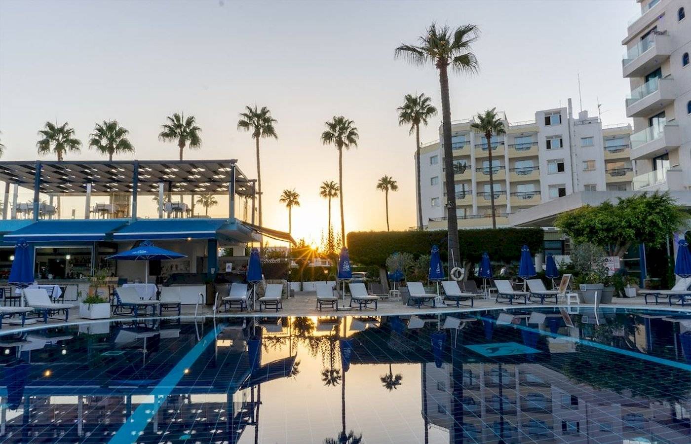 Sonnenuntergang am Swimmingpool des Anonymous Beach Hotels mit Lounge-Stühlen und Palmen.