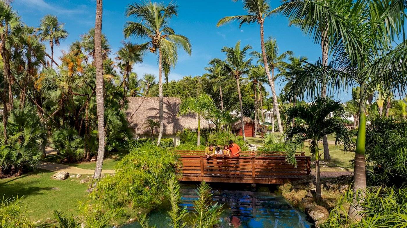 Familie auf einer Brücke im Sunscape Dominicus La Romana Hotel, umgeben von Palmen und Wasser.