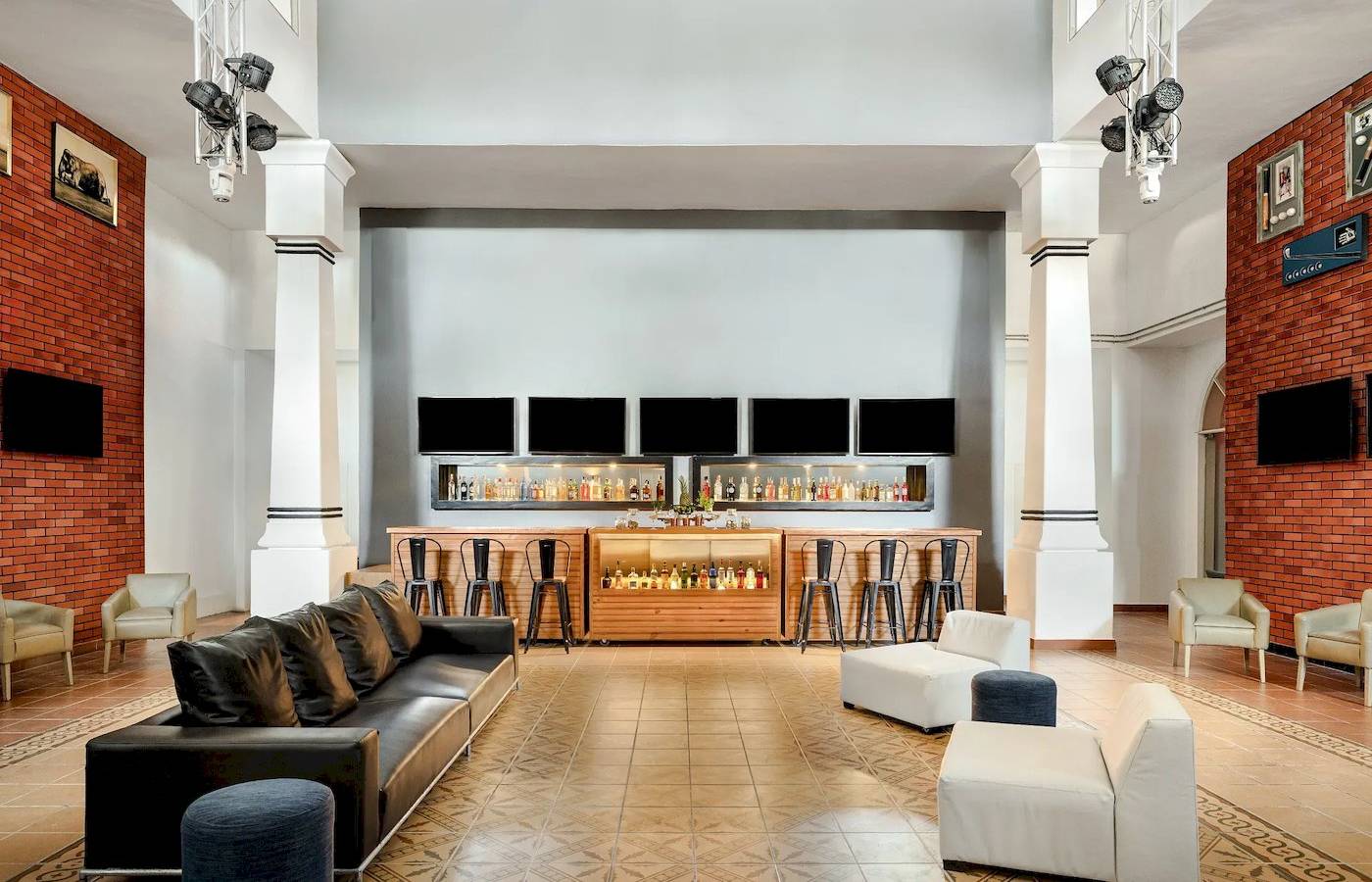 Lobby-Bar-Bereich des Sunscape Dominicus La Romana Hotels mit Bartheken, Sesseln und Fernsehgeräten.