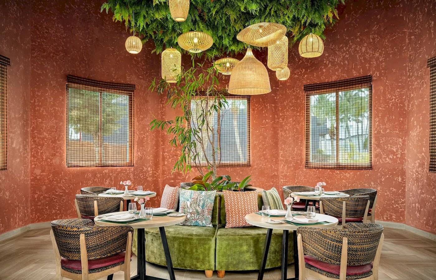 Innenansicht des Restaurants im Sunscape Dominicus La Romana Hotel mit grünem Sofa, Tisch, Pflanzen und hängenden Lampen.