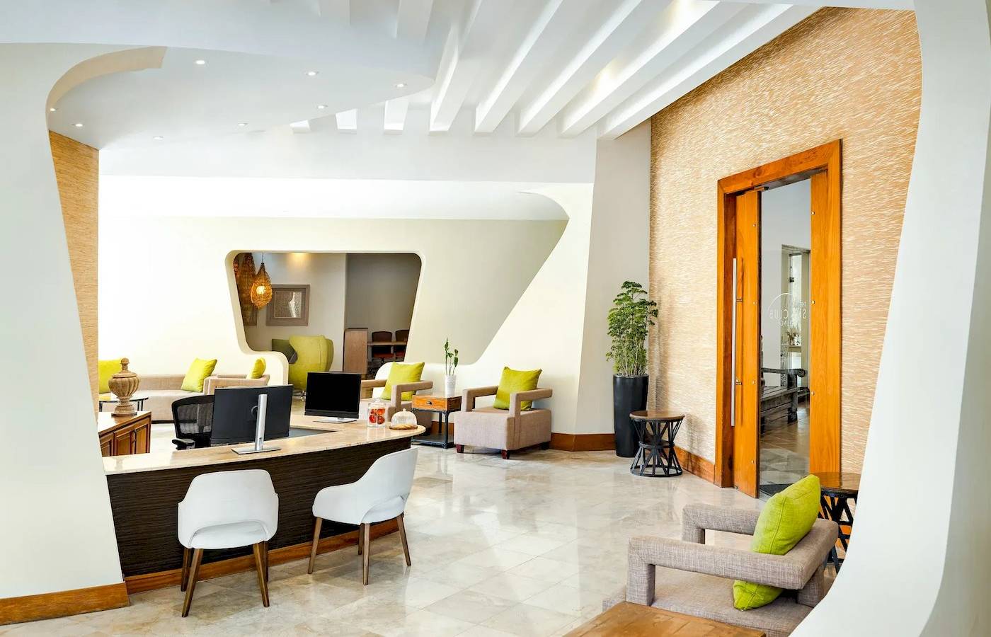 Innenraum des Hotels Sunscape Dominicus La Romana mit Rezeptionstresen, weißen Stühlen und grünen Kissen.