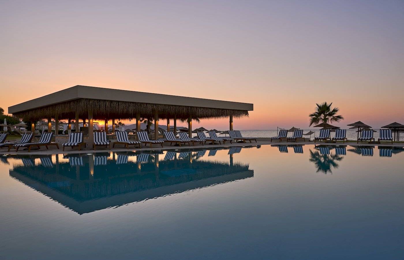 Atlantica Kalliston Resort Pool bei Sonnenuntergang mit Liegen und Sonnenschirmen