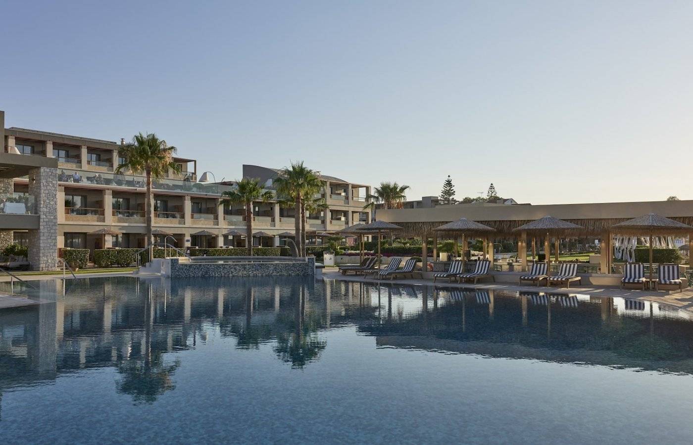 Außenpoolbereich des Atlantica Kalliston Resorts mit Lounge-Liegestühlen und Sonnenschirmen.