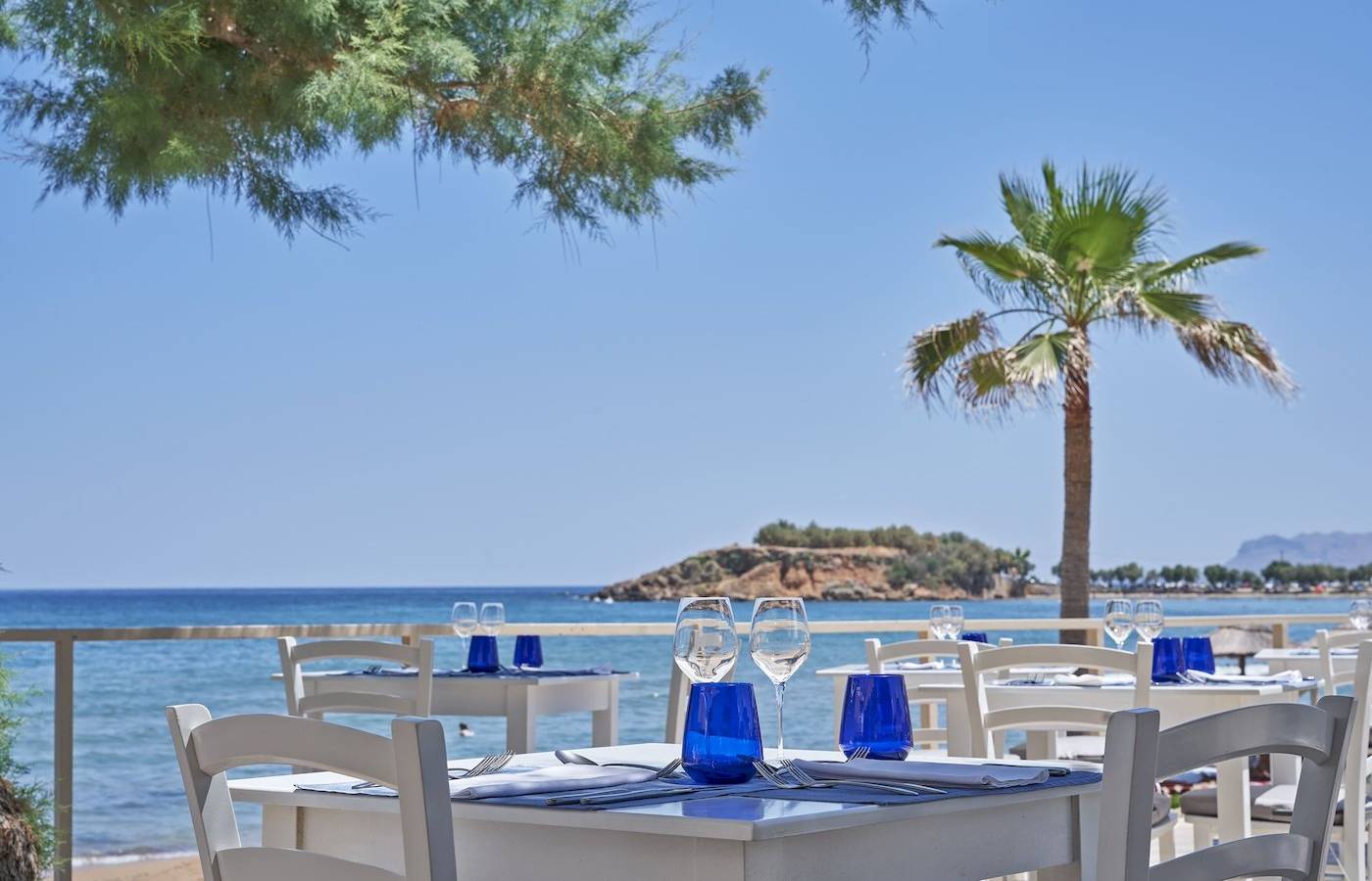 Terrasse des Atlantica Kalliston Resorts mit Tischen und Blick auf das Meer.