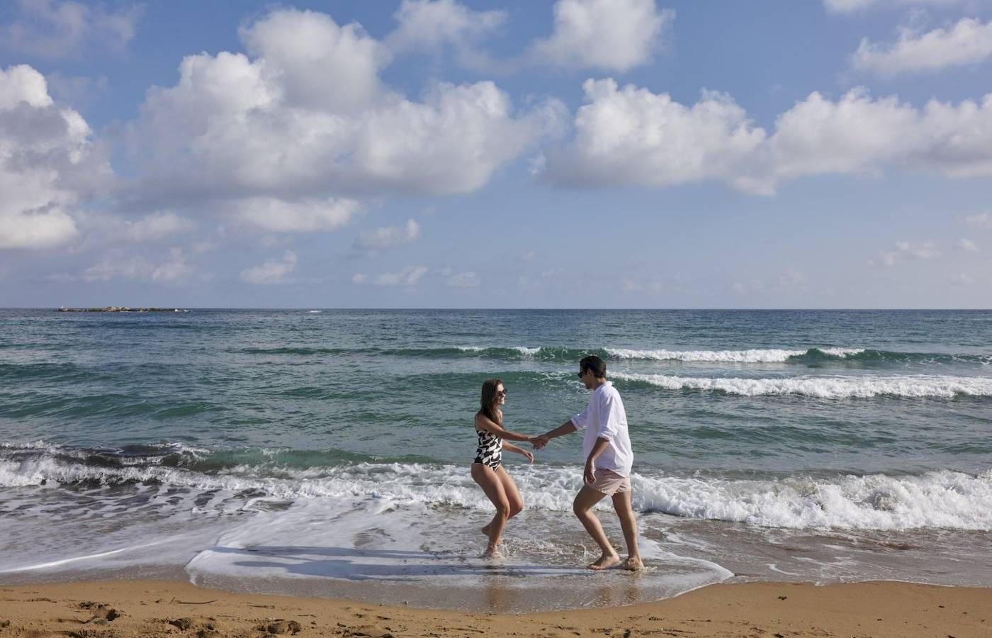 Paar im Wasser am Strand vor blauem Himmel mit Wellen und weißen Wolken